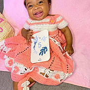 Maylee a rejoint le concours — aidez-le/la à gagner de superbes lots ! baby, child, crochet_dress, headband, pink, white, smiling, happy, card, holding, blanket, indoor, cute, infant, soft_texture, footwear, sitting, portrait, celebration, age_card