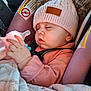 baby, infant, sleeping, car_seat, knit_hat, pom_poms, feeding_bottle, hand, blanket, seatbelt, car_interior, safety_warning_label, pink_clothing, chubby_cheeks, closed_eyes, adorable, cozy, profile, soft_texture, pacifier_clip
