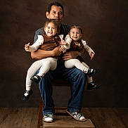Leyla is registered to the contest to win money with this photo: children, twins, father, family, portrait, studio, smiling, happy, sitting, holding, arms, brown_background, wooden_floor, chair, fashion, matching_outfits, toddler, girl, indoor, photography