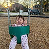Leyla is registered to the contest to win money with this photo: toddler, child, baby, swing, playground, smiling, happy, outdoor, sunset, suburban, house, trees, mulch, playground_equipment, swing_chains, pink_clothing, floral_pattern, sitting, portrait, joy