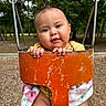 baby, child, infant, swing, playground, park, outdoor, portrait, smiling, happy, face, hands, blanket, yellow_clothing, orange_swing, rusty_metal, trees, nature, seated, close_up