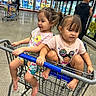 children, toddlers, siblings, shopping_cart, grocery_store, supermarket, freezer_aisle, shopping, sitting, smiling, faces, girls, pink_shirts, barefoot, cart_ride, indoors, retail, food, refrigerated_cases, family