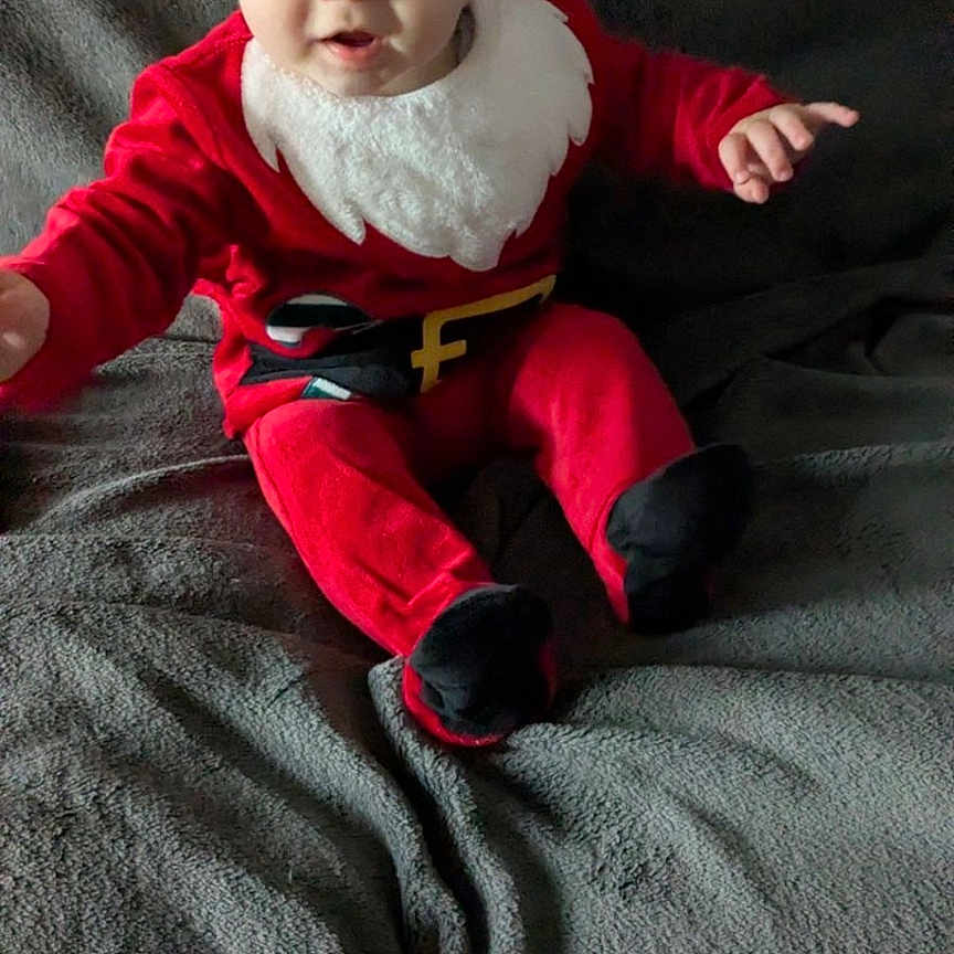 Gabriel a rejoint le concours — aidez-le/la à gagner de superbes lots ! baby, black_booties, blanket, child, christmas, cozy, cute, face, festive, holiday, indoor, infant, person, portrait, red_clothing, santa_hat, seasonal, sitting, smiling, young