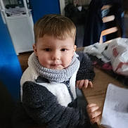 Gianny participe au concours pour gagner de l'argent avec cette photo : child, indoor, scarf, jacket, table, paper, scribbles, hand, face, hair, wood, chair, blurred, cozy, casual, person, young, sitting, clothing, home