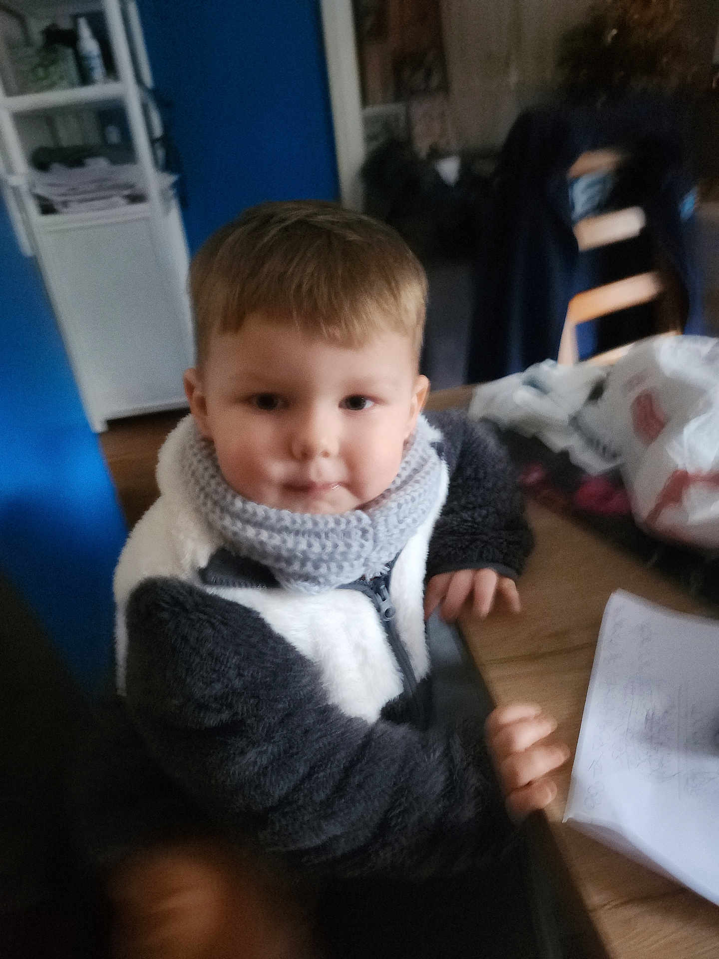 Gianny participe au concours pour gagner de l'argent avec cette photo : child, indoor, scarf, jacket, table, paper, scribbles, hand, face, hair, wood, chair, blurred, cozy, casual, person, young, sitting, clothing, home