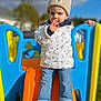 child, toddler, beanie, jacket, thumb_sucking, slide, playground, outdoor, blue, orange, yellow, jeans, sneakers, hand, sky, cloud, grass, daylight, person, toy