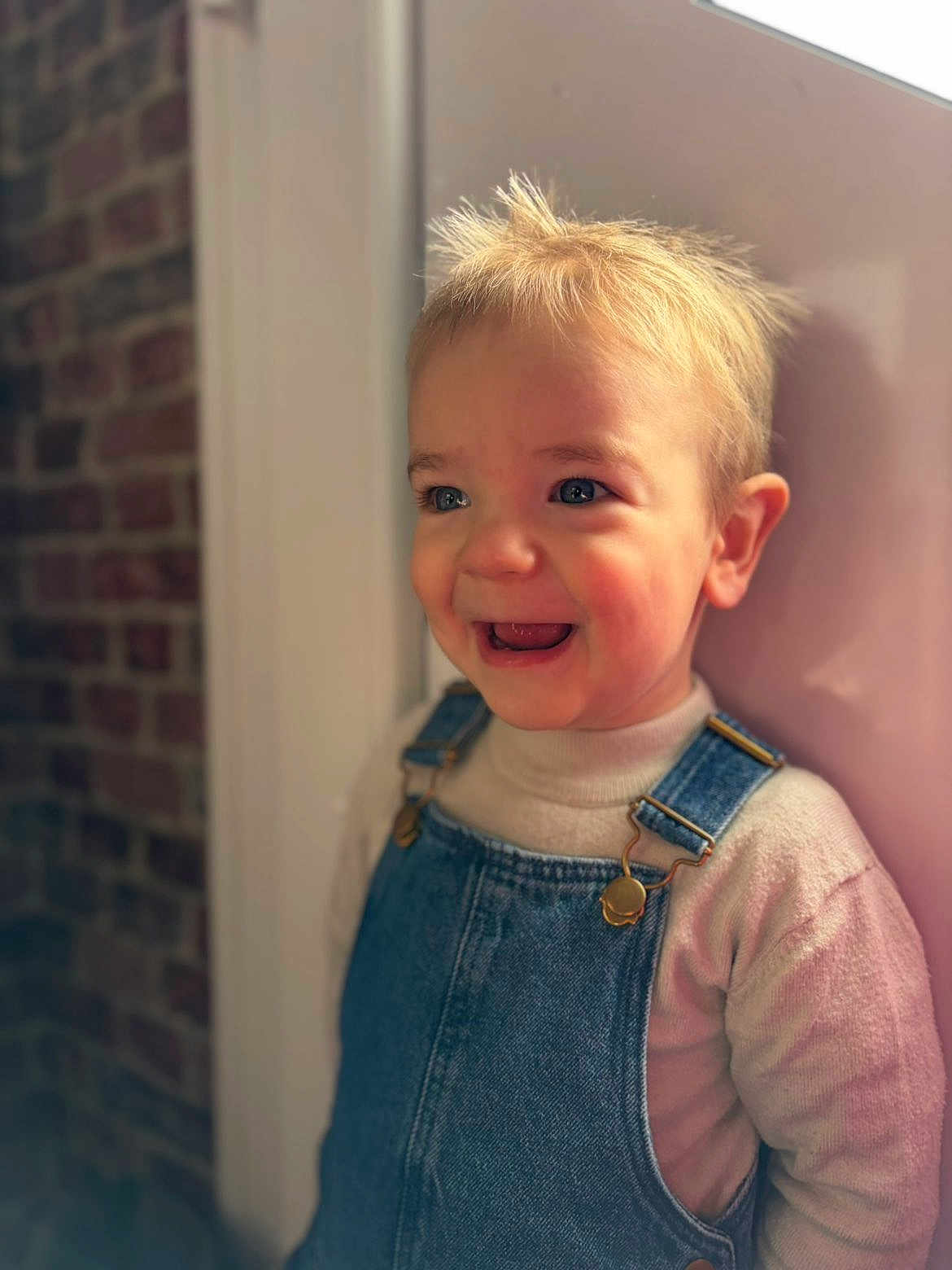 Sasha participe au concours pour gagner de l'argent avec cette photo : toddler, child, smiling, blue_eyes, blonde_hair, denim_overalls, sweater, portrait, indoor, brick_wall, happy, cute, young_child, face, person, clothing, fashion, casual, expression, light