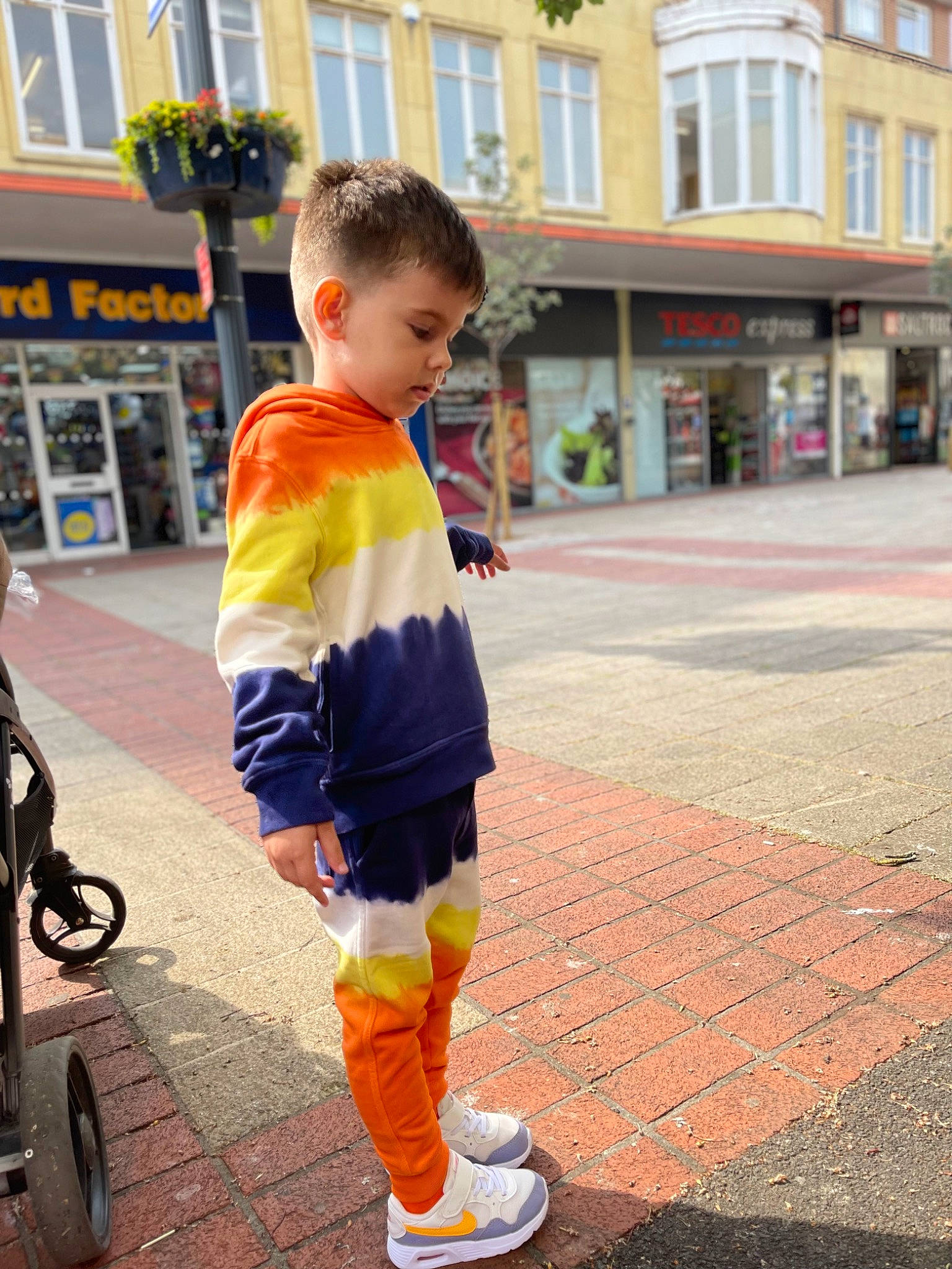 Darius is registered to the contest to win money with this photo: asphalt, building, cool, fun, happy, leg, orange, person, recreation, shoe, shorts, sidewalk, sleeve, standing, t_shirt, tire, toddler, travel, wheel, window