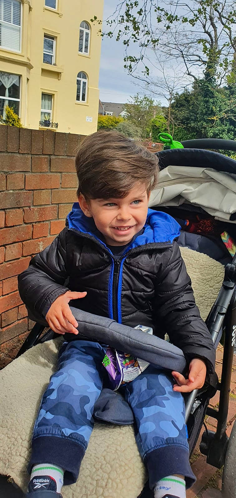 Darius is registered to the contest to win money with this photo: baby_carriage, baby_products, brick, brickwork, child, electric_blue, fun, grass, hoodie, joy, leisure, person, recreation, sitting, sky, toddler, tourism, travel, tree, windbreaker