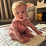 baby, child, infant, sitting, pink_onesie, soft_mat, curly_hair, blue_eyes, indoors, carpet, basket, flowers, folded_clothes, baby_clothing, cute, chubby_cheeks, floor, home, portrait, curious