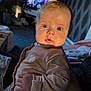 Myla-Mae is registered to the contest to win money with this photo: baby, infant, face, blue_eyes, clothing, heart, indoor, living_room, television, carpet, patterned_wallpaper, hand, soft_light, curious, person, portrait, cozy, child, cute, young