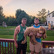 Chester is registered to the contest to win money with this photo: man, dog, backyard, deck, fence, grass, tree, sunset, house, playground, smile, glasses, tank_top, shorts, pet, tongue_out, outdoor, friendship, casual, nature
