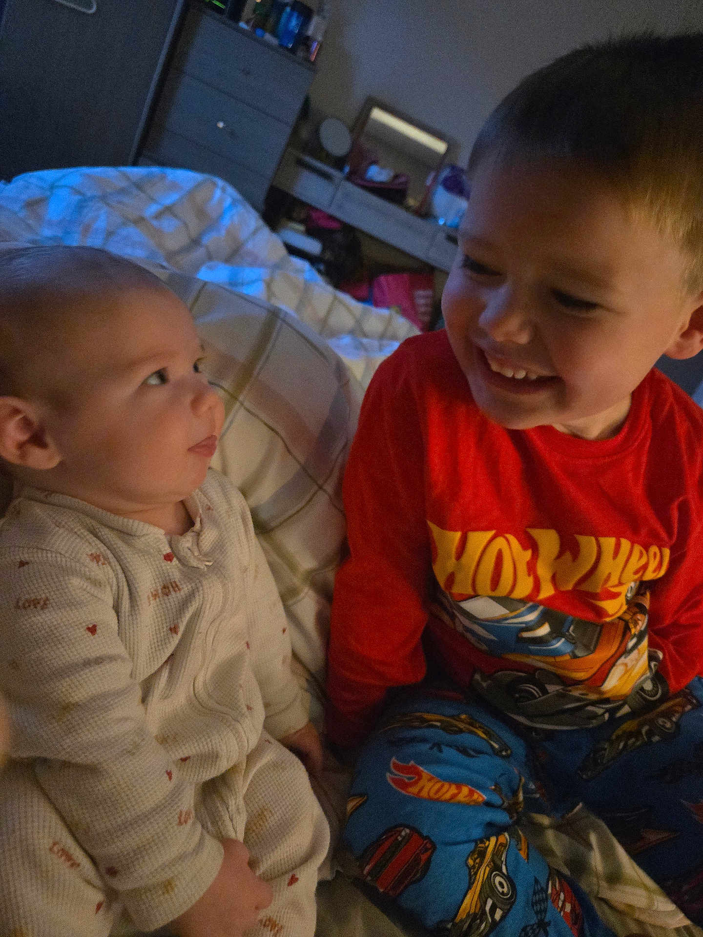 Cillian is registered to the contest to win money with this photo: baby, child, pajamas, bed, smile, face, indoor, sibling, happy, person, clothing, blanket, furniture, room, head, cute, expression, toy, warm_lighting, cozy