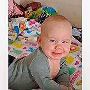 Elias is registered to the contest to win money with this photo: baby, smile, face, infant, blanket, patterned_blanket, colorful, rainbow, heart, clothing, onesie, lying_down, indoors, cheeky, cute, child, person, toddler, happy, portrait