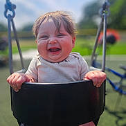 Lillith joined the competition — help win amazing prizes! baby, child, swing, playground, smiling, happy, outdoor, sunny, grass, hands, face, clothing, black_swing, hair, infant, summer, fun, joy, person, park