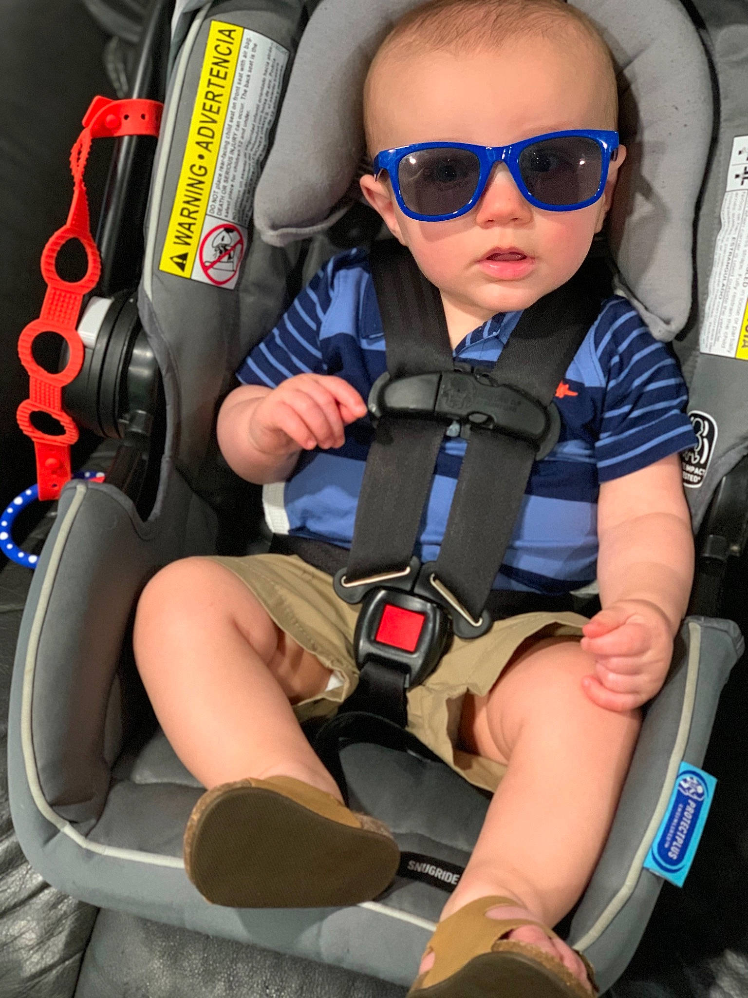 Santino is registered to the contest to win money with this photo: auto_part, car_seat, comfort, eyewear, glasses, goggles, human_leg, leg, person, product, recreation, seat_belt, shoe, shorts, sneakers, sunglasses, thigh, toddler, vision_care, white