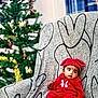 baby, child, infant, red_clothing, hat, armchair, patterned_fabric, christmas_tree, holiday, decorations, tinsel, ornaments, indoor, festive, cute, portrait, seated, young_child, soft_lighting, cozy
