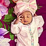 Janice is registered to the contest to win money with this photo: baby, sleeping, pink_outfit, headband, bow, floral_blanket, infant, peaceful, cute, soft_texture, closeup, portrait, child, resting, adorable, small_hands, cozy, indoors, colorful, babywear