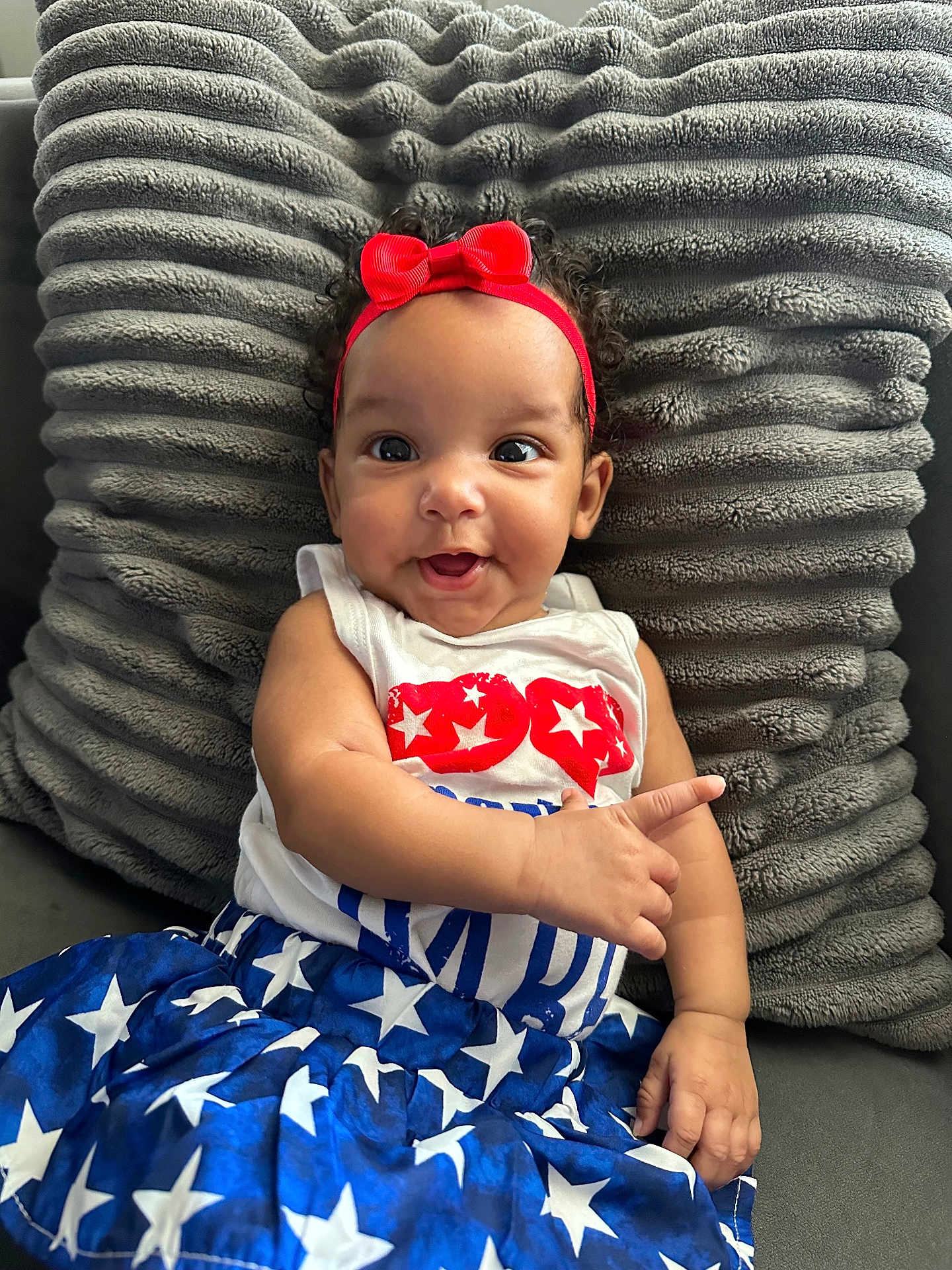 Nalani joined the competition — help win amazing prizes! baby, child, smiling, headband, red_bow, dress, stars, white, blue, red, pillow, plush, couch, happy, portrait, person, infant, cute, indoor, clothing