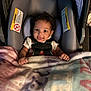 Nalani is registered to the contest to win money with this photo: baby, car_seat, blanket, child, smiling, face, curly_hair, seatbelt, infant, clothing, indoors, cute, portrait, happy, comfort, soft, young_child, hands, head, person