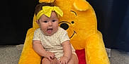 Lyla is registered to the contest to win money with this photo: baby, child, plush_chair, winnie_the_pooh, yellow_headband, carpet, indoor, happy, smiling, seated, cute, infant, toy_chair, person, face, clothing, playful, background, fabric, curtain
