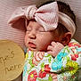 Christlynn is registered to the contest to win money with this photo: newborn, baby, sleeping, headband, pink, bow, floral_blanket, wooden_sign, text, closeup, portrait, infant, peaceful, cute, soft_light, indoors, pink_background, hand, face, resting