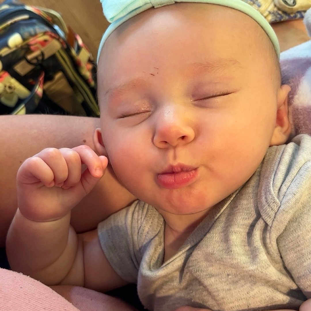 Christlynn is registered to the contest to win money with this photo: arm, baby, background, blue_bow, child, closed_eyes, cute, face, gray_clothing, hand, headband, indoor, infant, person, pink, puckered_lips, resting, skin, soft_surface, wood_floor