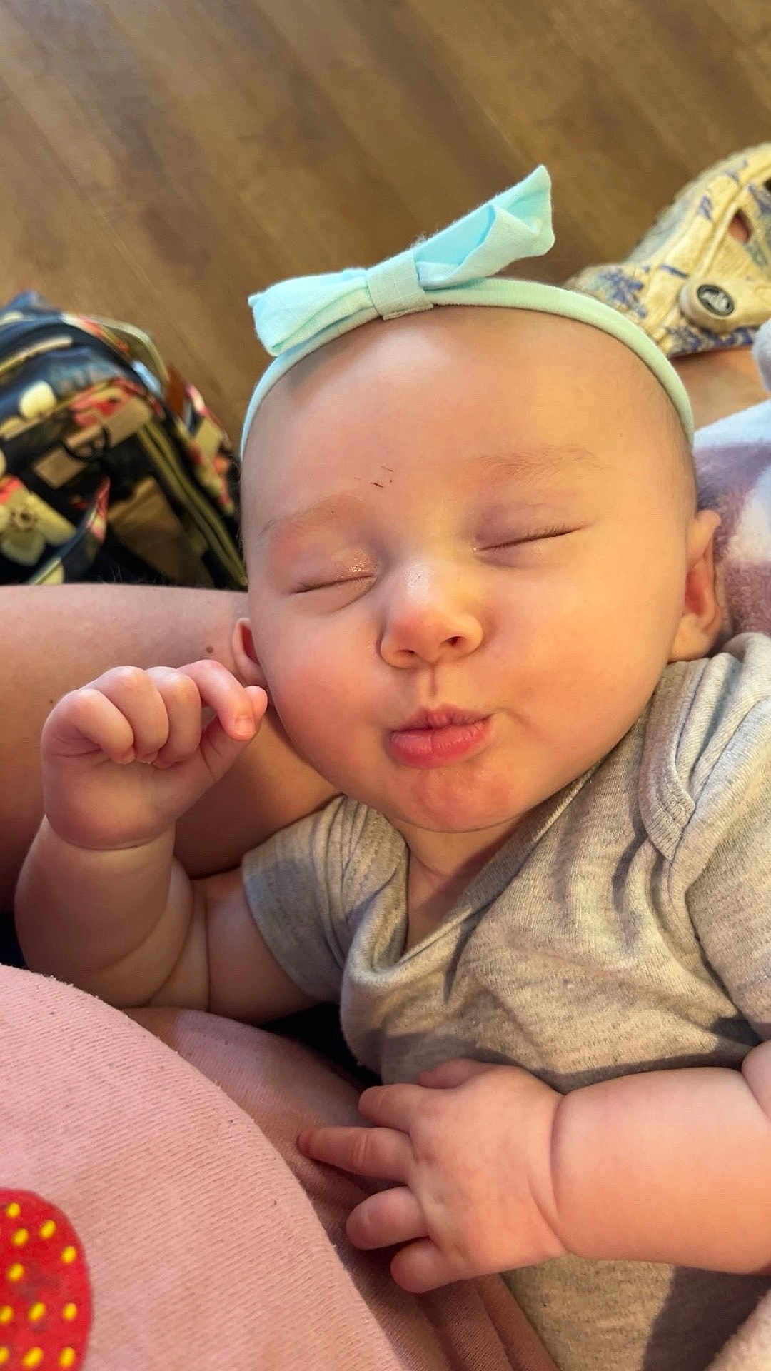 Christlynn is registered to the contest to win money with this photo: baby, infant, headband, blue_bow, closed_eyes, puckered_lips, hand, arm, gray_clothing, soft_surface, pink, indoor, wood_floor, background, cute, child, person, skin, face, resting
