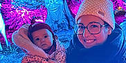 Emie-Rose participe au concours pour gagner de l'argent avec cette photo : baby, woman, glasses, knitted_hat, scarf, winter_clothing, outdoor, night, colorful_lights, tree_sculpture, face_art, smile, holding, portrait, child, person, forest, decoration, festival, family