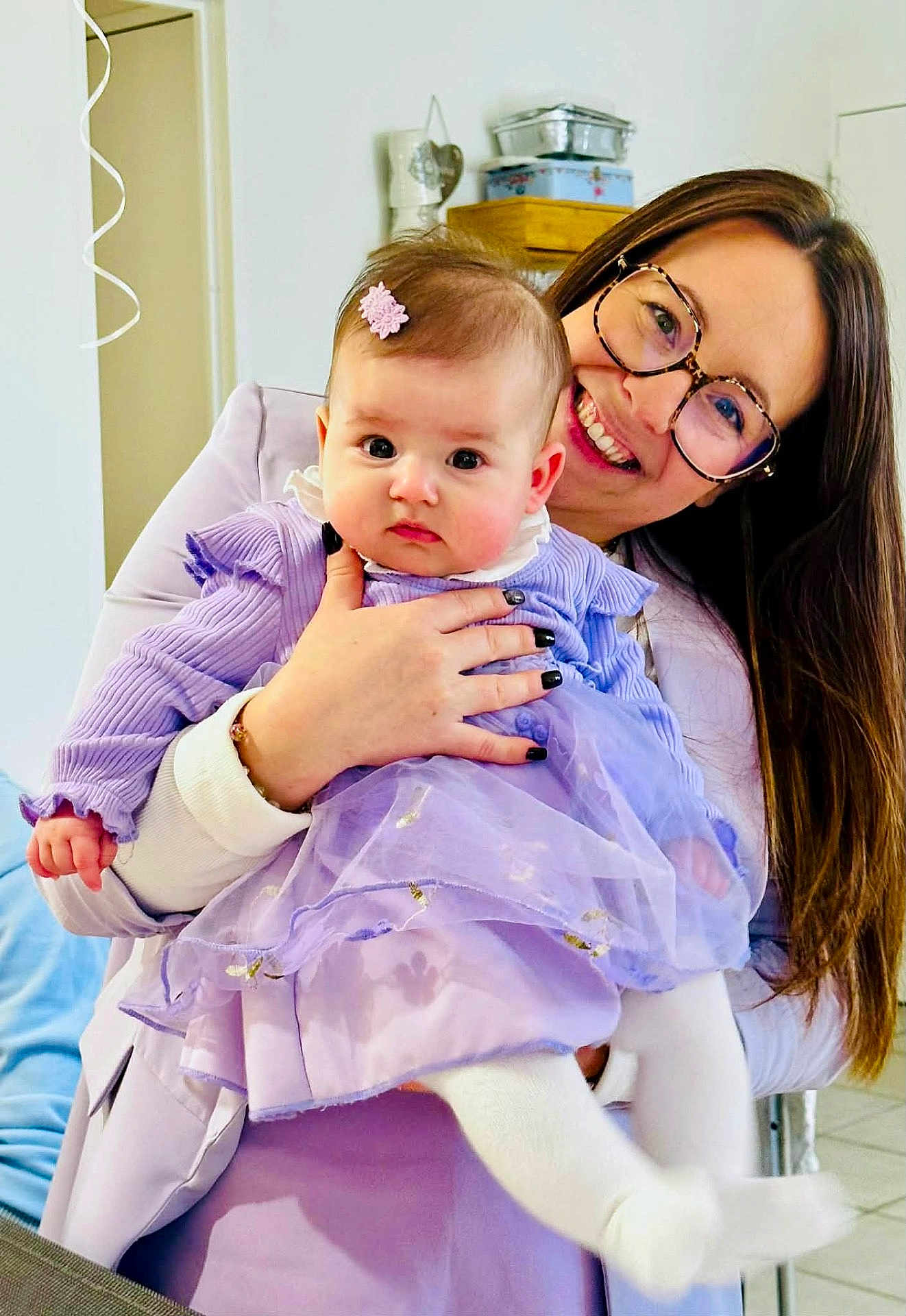 Emie-Rose a rejoint le concours — aidez-le/la à gagner de superbes lots ! baby, woman, glasses, holding, dress, lavender, indoor, smile, hair_clip, person, child, happy, long_hair, furniture, home, cute, fashion, portrait, white_tights, hand