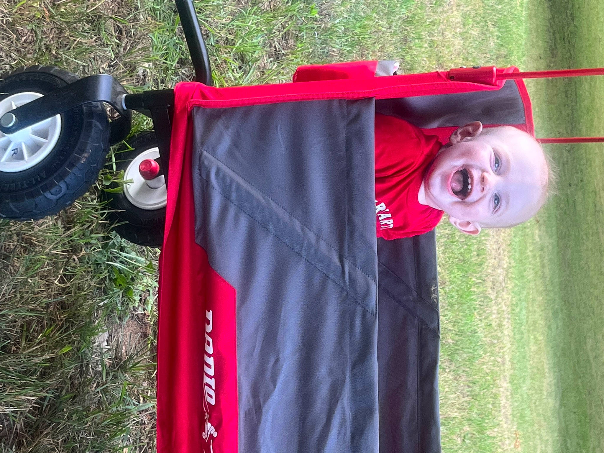 Declan is registered to the contest to win money with this photo: automotive_tire, baby, baby_products, baby_toddler_clothing, carmine, costume, electric_blue, event, flag, grass, magenta, pattern, person, red, sleeve, smile, sportswear, t_shirt, tire, toddler