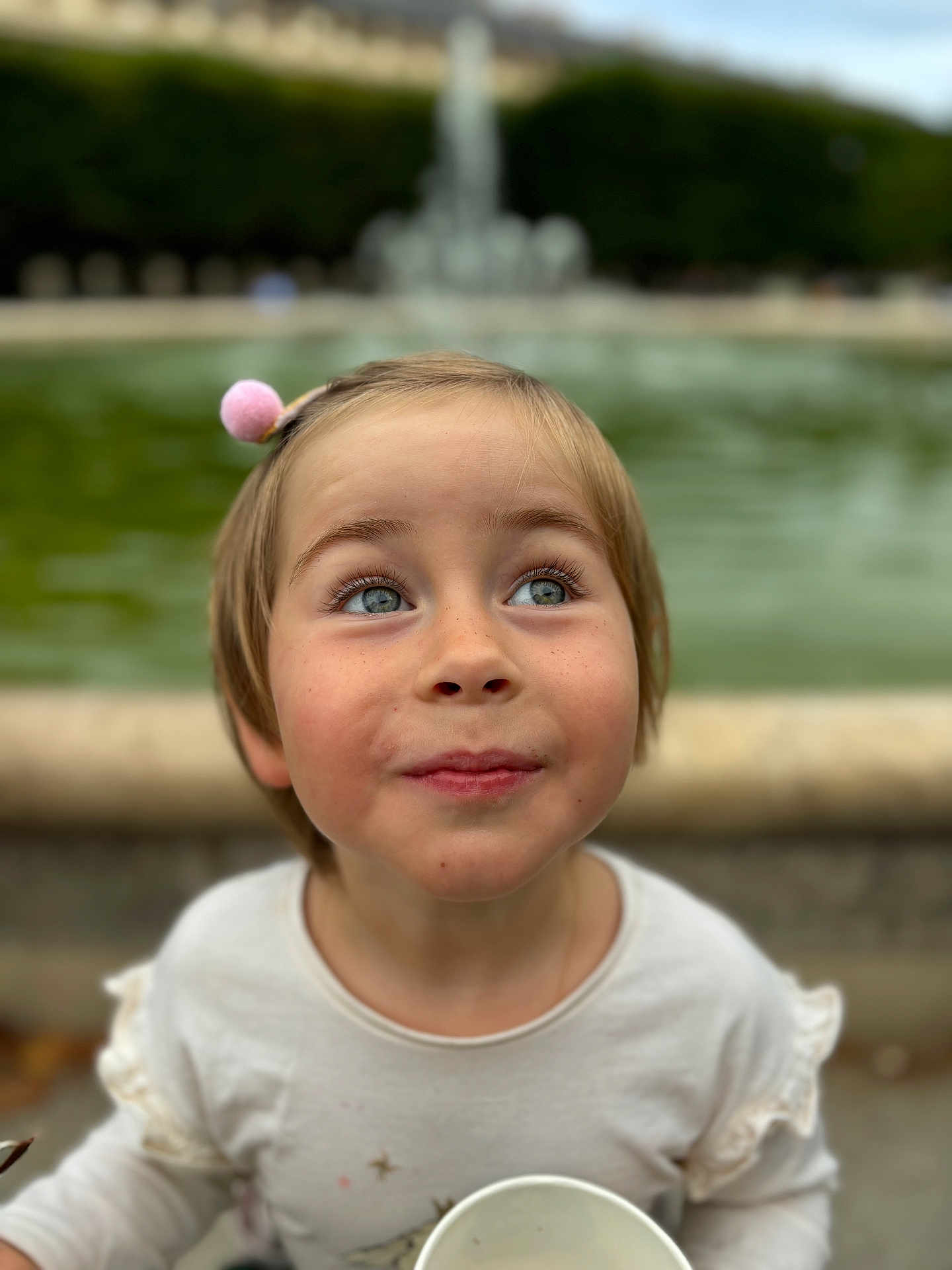 Mathilde a rejoint le concours — aidez-le/la à gagner de superbes lots ! child, portrait, blue_eyes, smile, hairpin, cup, outdoor, fountain, blurred_background, curious, cute, casual_clothing, young_child, daylight, happy, face, innocent, freckles, short_hair, nature