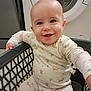 appliance, baby, child, clothing, cute, domestic, fabric, face, happy, home, indoor, infant, laundry_basket, onesie, pattern, person, playful, sitting, smiling, washing_machine