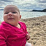 baby, child, smiling, pink_sweater, beach, pebbles, sea, cloudy_sky, happy, cute, portrait, outdoor, person, infant, face, clothing, nature, sitting, daylight, casual