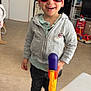 child, boy, sunglasses, toy_gun, indoor, smiling, hoodie, casual_clothing, shoes, carpet, stairs, toy, home, person, happy, short_hair, light, floor, door, furniture