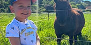 élyo a rejoint le concours — aidez-le/la à gagner de superbes lots ! child, boy, smiling, cap, tshirt, pony, animal, grass, field, fence, sunny, outdoor, nature, greenery, daylight, portrait, happy, casual_clothing, trees, sky