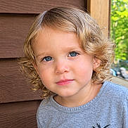 Mason joined the competition — help win amazing prizes! blonde_hair, blue_eyes, california, child, close_up, curly_hair, face, greenery, headshot, looking_at_camera, natural_light, outdoor, palm_tree, person, photography, portrait, serious_expression, shirt, toddler, wooden_siding