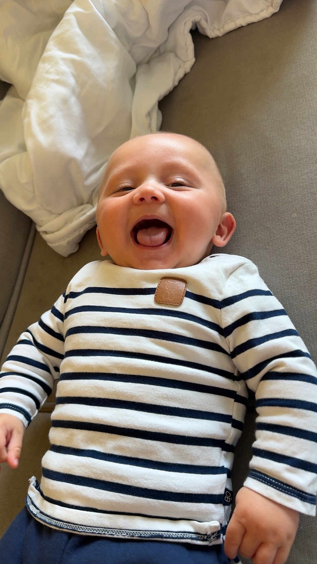 Ezeckiel participe au concours pour gagner de l'argent avec cette photo : baby, child, smile, happy, striped_shirt, couch, indoor, infant, person, cute, portrait, young, sleeve, clothing, hand, face, skin, head, mouth, joy