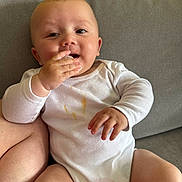 Ezeckiel a rejoint le concours — aidez-le/la à gagner de superbes lots ! baby, child, infant, onesie, white_clothing, couch, sofa, hand, face, skin, chewing, sitting, indoors, cute, expression, messy_clothing, furniture, comfort, young, portrait