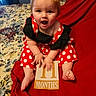 baby, bright_colors, celebration, child, cute, dress, face, feet, hands, happy, indoor, infant, milestone_card, person, polka_dot, portrait, red_blanket, sitting, smiling, young_child