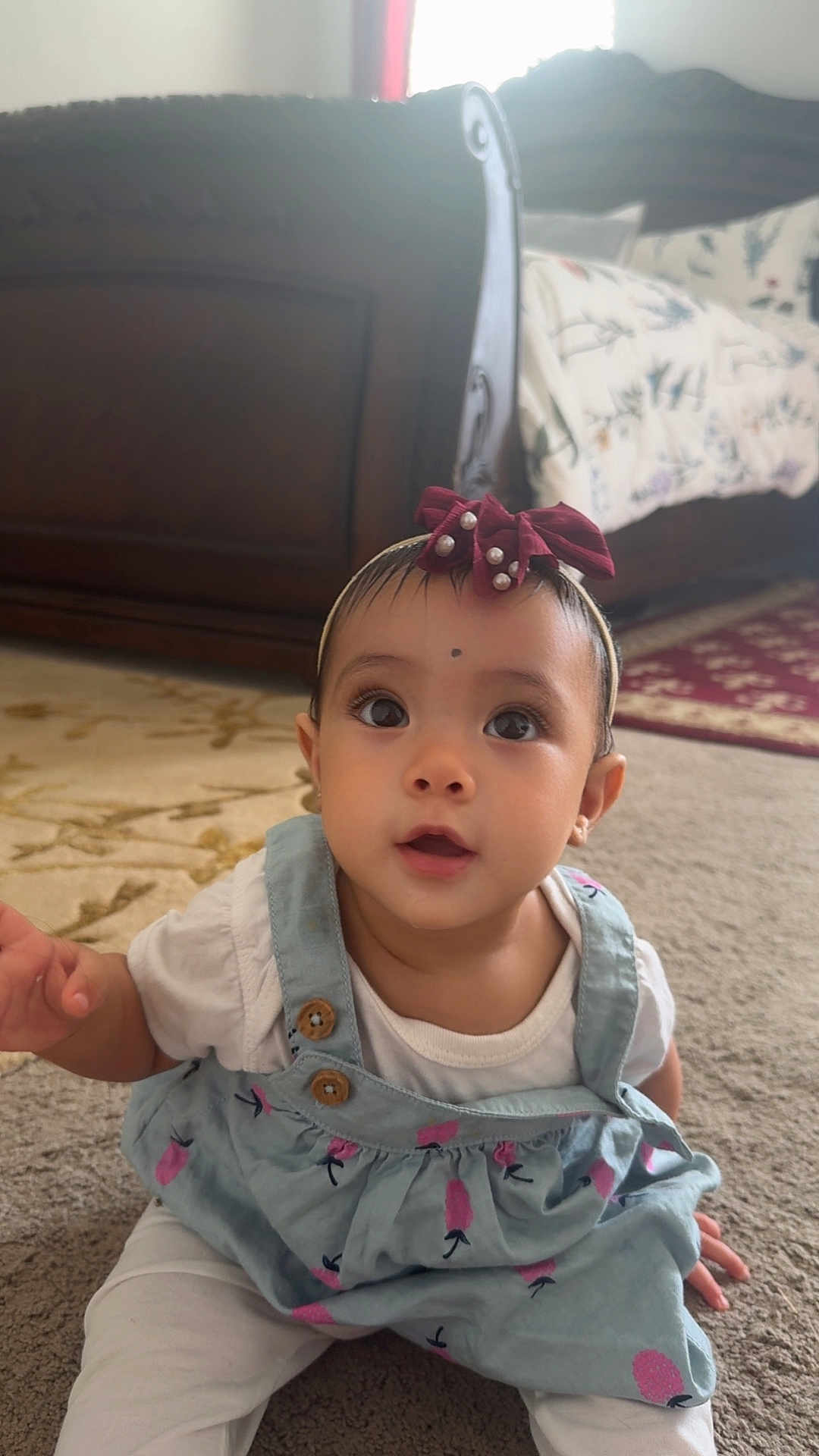 Devyani joined the competition — help win amazing prizes! baby, big_eyes, carpet, child, curious, cute, cute_baby, dress, floor, headband, home, indoor, infant, looking_up, patterned_clothing, person, portrait, sitting, white_clothing, young_child
