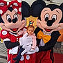 baby, child, costume, character, mascot, mickey_mouse, minnie_mouse, red_dress, yellow_bow, white_gloves, outdoor, tent, pavement, people, portrait, event, fun, cute, smiling_characters, serious_baby
