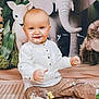 baby, cake, messy, smiling, face, white_shirt, brown_pants, stuffed_elephant, stuffed_lamb, stuffed_monkey, floor_mat, food, cream, celebration, child, indoor, playful, cute, portrait, sitting