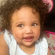 Carmen is registered to the contest to win money with this photo: toddler, child, curly_hair, smiling, happy, face, skin, arm, white_clothing, indoor, baby, person, cute, portrait, infant, expression, young_child, close_up, soft_lighting, cozy