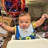 Theodore joined the competition — help win amazing prizes! baby, high_chair, bib, food_stains, arms_raised, spiderman_balloon, balloon, living_room, couch, cardboard_box, table, cute, child, indoor, person, smiling, happy, home, furniture, celebration
