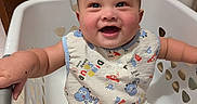 Theodore is registered to the contest to win money with this photo: baby, child, laundry_basket, smiling, happy, dinosaur_print, clothing, indoor, cute, infant, person, portrait, sitting, short_sleeve, playful, hair, cheeks, expression, room, door
