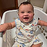 baby, child, laundry_basket, smiling, happy, dinosaur_print, clothing, indoor, cute, infant, person, portrait, sitting, short_sleeve, playful, hair, cheeks, expression, room, door
