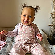 Zephyra joined the competition — help win amazing prizes! baby, child, smile, pigtails, pink_clothing, flower_pattern, sitting, indoor, happy, cute, infant, person, face, hands, playful, cozy, changing_pad, soft_lighting, wall, fabric