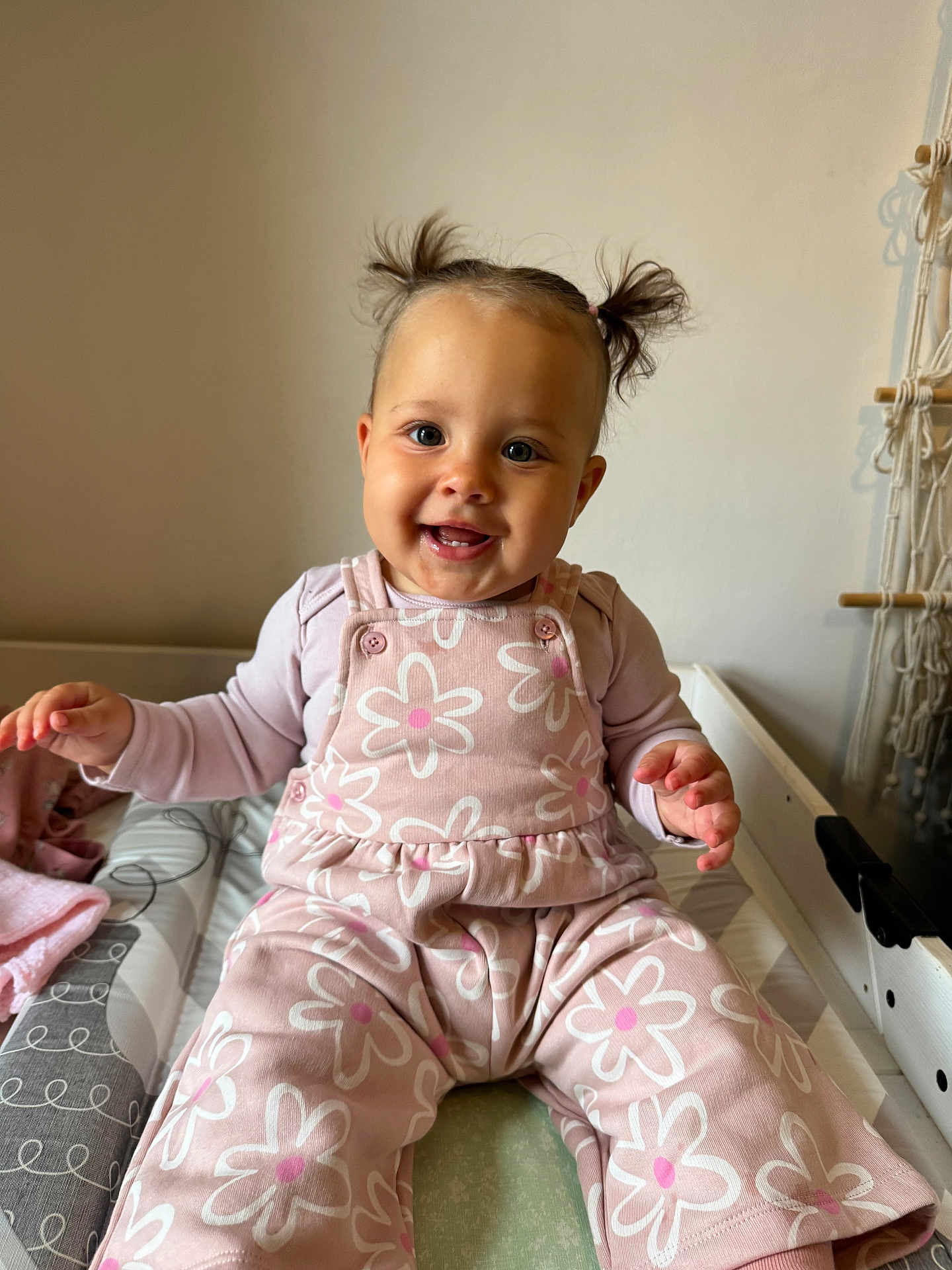 Zephyra joined the competition — help win amazing prizes! baby, child, smile, pigtails, pink_clothing, flower_pattern, sitting, indoor, happy, cute, infant, person, face, hands, playful, cozy, changing_pad, soft_lighting, wall, fabric