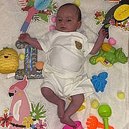 Aylan participe au concours pour gagner de l'argent avec cette photo : baby, infant, blanket, toy, pink_bucket, green_shovel, orange_rake, blue_octopus_toy, green_dinosaur_toy, colorful_birds, pom_poms, white_clothing, cute, child, playtime, indoors, soft_texture, portrait, lying_down, decorations